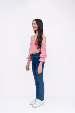 45 degree angled shot of a slim asian trans woman. Wearing a light pink off-shoulder blouse, jeans and white sneakers. Whole body photo on a white background.
