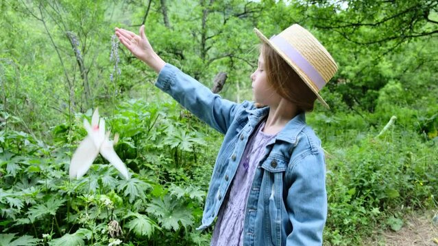 A 9-year-old girl in a hat launches a paper bird into the air in nature.