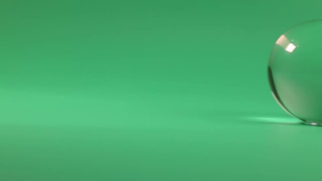 transparent glass crystal ball rolling traveling over green surface background