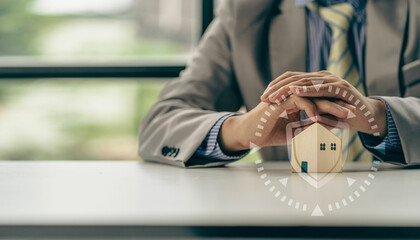 Symbol of property and safety insurance Close-up of a house model on a table and a human hand above it. With home insurance concept icons