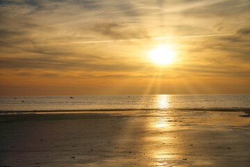 Fototapeta na wymiar Sunset, illuminated sea. Sandy beach in the foreground. Light waves. Baltic Sea