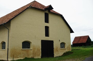 Beige Fassade von altem verwittertem Stallgebäude mit braunem Holztor vor altem Stall auf grüner...