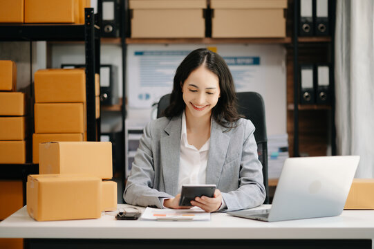 Startup small business SME, Entrepreneur owner woman using smartphone or tablet taking receive and checking online purchase shopping order to preparing pack product box. ..