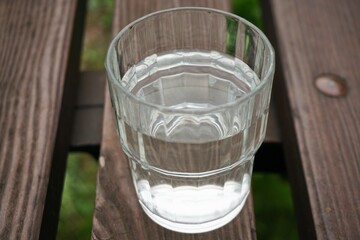 Glas Wasser auf brauner Holzbank über grüner Wiese am Nachmittag im Sommer
