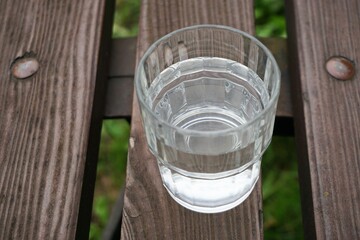 Volles Glas Wasser auf alter brauner Holzbank über Wiese am Nachmittag im Sommer