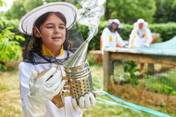 Girl as beekeeper with bee smoker in front of bee hives