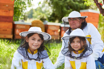 Smiling girls with male apiarist wearing protective suits - Powered by Adobe