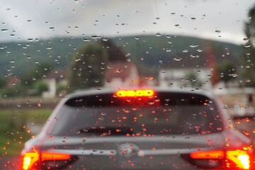 Regentropfenmuster auf Glasscheibe vor Auto mit orange-roten Lichtern auf Fähre über Fluss und...