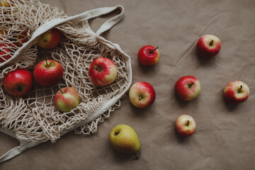 Red apples in a eco mesh shopping bag on a paper background. Zero waste, no plastic. Autumn flatlay