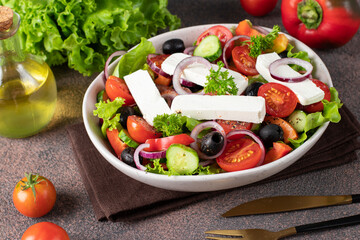 Classic Greek salad from tomatoes, cucumbers, sweet pepper, olives, red onion and feta cheese in white bowl