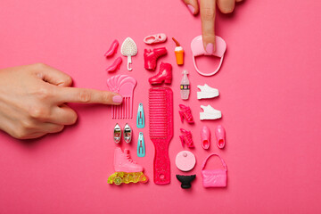 Doll accessories and female hands on pink background, top view