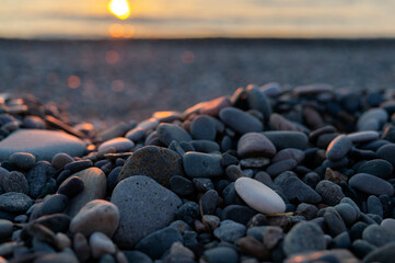 Pebbles lit by the setting sun. Blurred sea in the background. Copy space.
