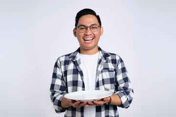 Happy young Asian man in casual shirt holding empty blank plate isolated on white background