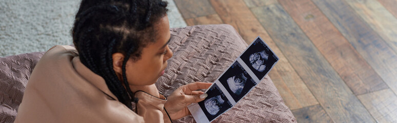 top view of african american woman lying on bed, looking at ultrasound, abortion concept, banner