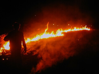 Silhouette of a guy standing against the background of burning grass at night	
