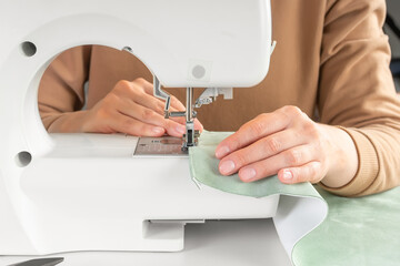 Obraz na płótnie Canvas Tailor hands stitching green fabric on modern sewing machine at workplace in atelier. Women's hands sew pieces of fabric on sewing machine closeup. Handmade, hobby, repair, small business concept