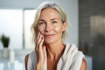 Papier Peint photo Spa Headshot of gorgeous mid age adult 50 years old blonde woman standing in bathroom after shower touching face, looking at reflection in mirror doing morning beauty routine. Older skin care concept.