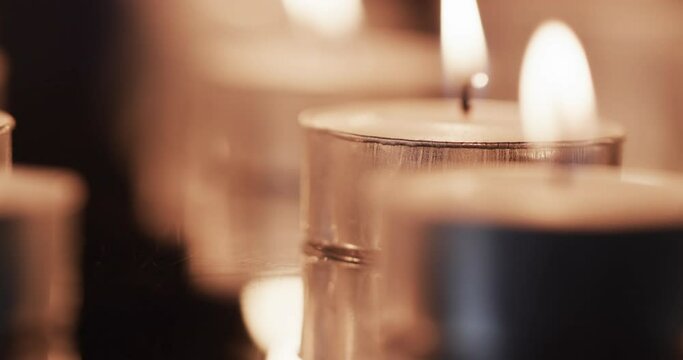 Video of close up of rows of tea candles with white flames and copy space on black background