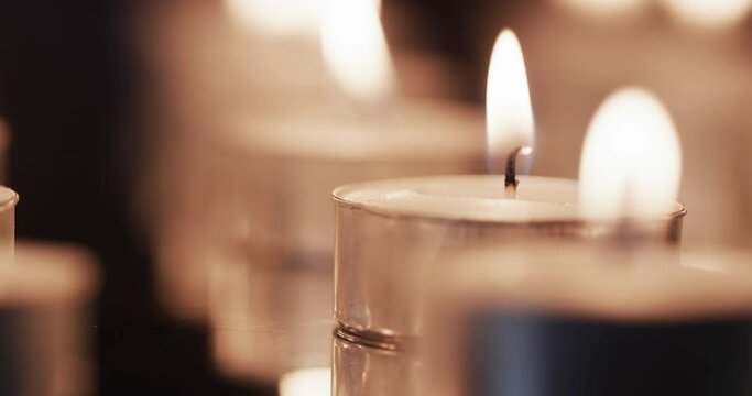 Video of close up of rows of tea candles with white flames and copy space on black background