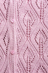 Handmade pink knitting wool texture background with knitted leaf shapes. Part of cardigan with buttons. Top view of knitting clothes