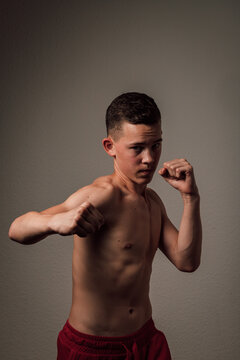 A teenage boxer athlete is training to box on dark background. Aggressive sport
