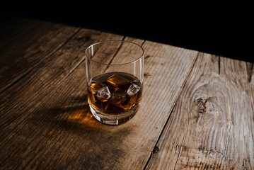 Close up of glass of bourbon whiskey with ice cubes on old wooden table isolated on black