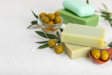 Natural bar of soap with olive oil extract on white textured wood. Pieces of green nourishing soap and olive berries. Body care and spa concept. Place for text.Copy space.Flat lay