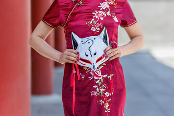 A young Asian girl walks in national clothes with a white mask in the park. Chinese woman in a red...