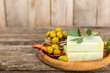 Natural bar of soap with olive oil extract on brown textured wood. Pieces of green nourishing soap and olive berries. Body care and spa concept. Place for text.Copy space.Flat lay