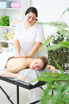 masseur massages the back, lower back, shoulders and neck of a young woman against the background of a bright office and greenery.