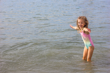 Beautiful happy little girl playing in the waves and splashes on the sea