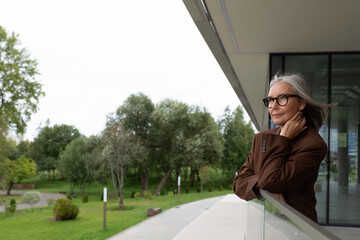 well-groomed elderly gray-haired business woman in a brown jacket and trousers is waiting for a business partner on the street