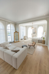 cozy bright apartment with huge panoramic windows with sunlight. bedroom in white and beige tones with fireplace and soft armchair. stylish living room with log coffee table and large white sofa