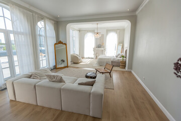 Fototapeta na wymiar cozy bright apartment with huge panoramic windows with sunlight. bedroom in white and beige tones with fireplace and soft armchair. stylish living room with log coffee table and large white sofa
