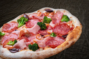 Pizza with salami, ham, vienna sausages, kalamata, olives, broccoli, pelati, pesto. Neapolitan round pizza on wood background