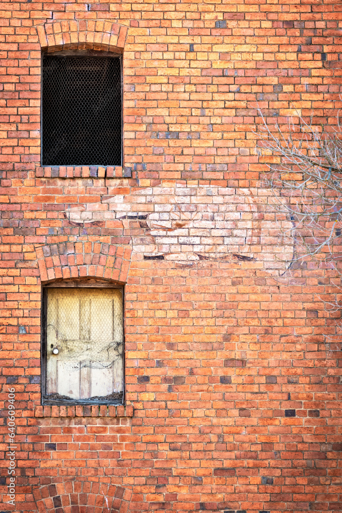 Wall mural side of an old brick building with two windows, one empty and one boarded, with a faded old sign of 