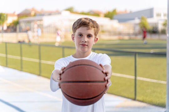 Teenage boy holding and showing basketball ball while posing outdoors. Sports concept.