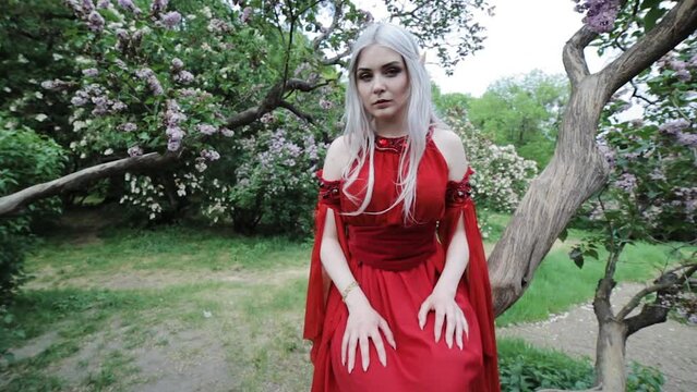 A beautiful elf woman dressed in a red dress is sitting on a tree in the forest.