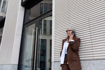 mature business woman with gray hair dressed in a brown suit walks around the city