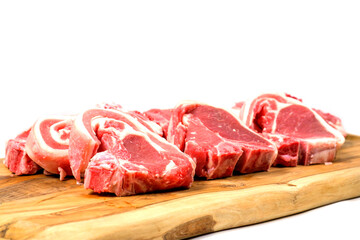 Stack of fresh lamb loin chops on wooden cutting board and on white surface. Premium high quality red meat. Butcher craft. Uncooked product.