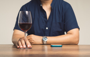 Businessman's right hand touches the base of a glass of red wine while sitting at the table