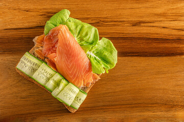 rye diet toast with salmon, sliced cucumber and lettuce on wooden surface top view