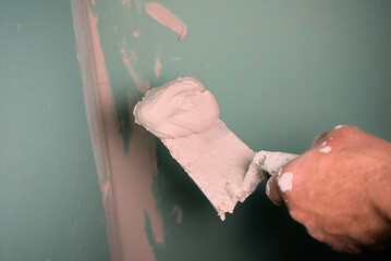 Hand with a spatula. Worker trowels putty on drywall. Puttying plasterboard walls with a spatula...