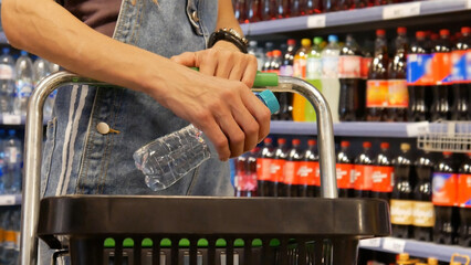 Close-up of a young woman's hands putting a bottle of water into a shopping cart