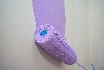 Painting a concrete wall with geometric shapes inside a house with water-based paint using a paint roller