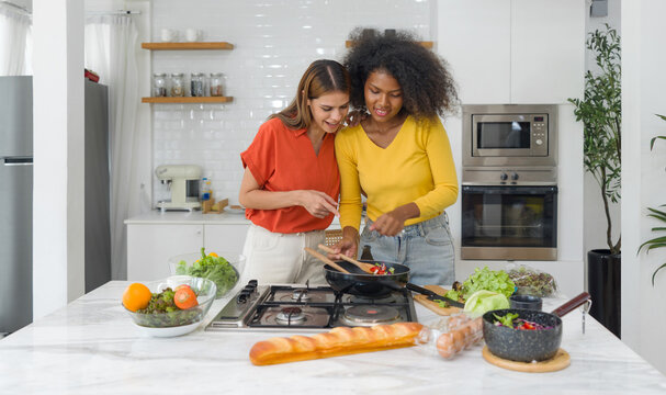 A vibrant shared moment in the heart of home, as two women infuse love into food they prepare in a sunlit kitchen.