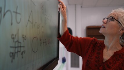 Closeup of happy female teacher writing on an interactive whiteboard teaching geometry math in a school classroom.