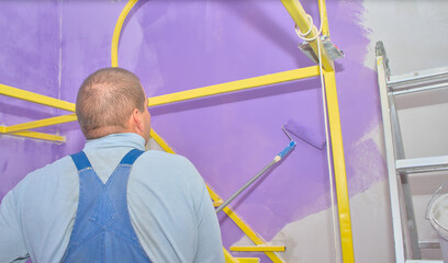 A man paints on a concrete wall inside a house with water-based paint using a paint roller.