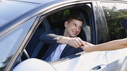 Car dealer giving key to new car owner. Businessman sitting behind steering wheel at car. Happy man taking car key from dealer in auto show or salon. Driving, safety and people concept.