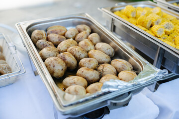 A silver tray filled with baked potatoes at a barbecue buffet